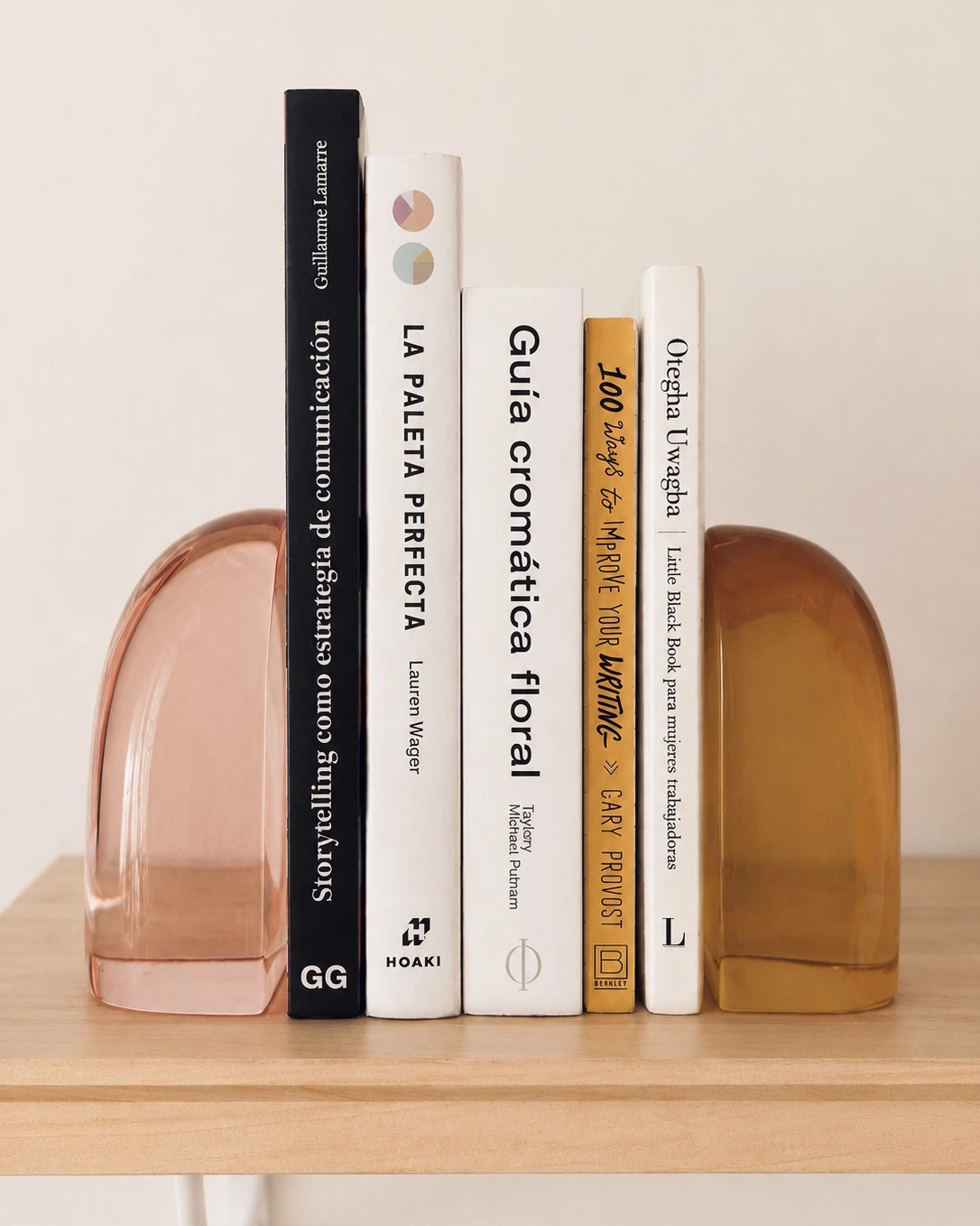 Libros de diseño, color y comunicación entre sujetalibros de cristal sobre estante de madera